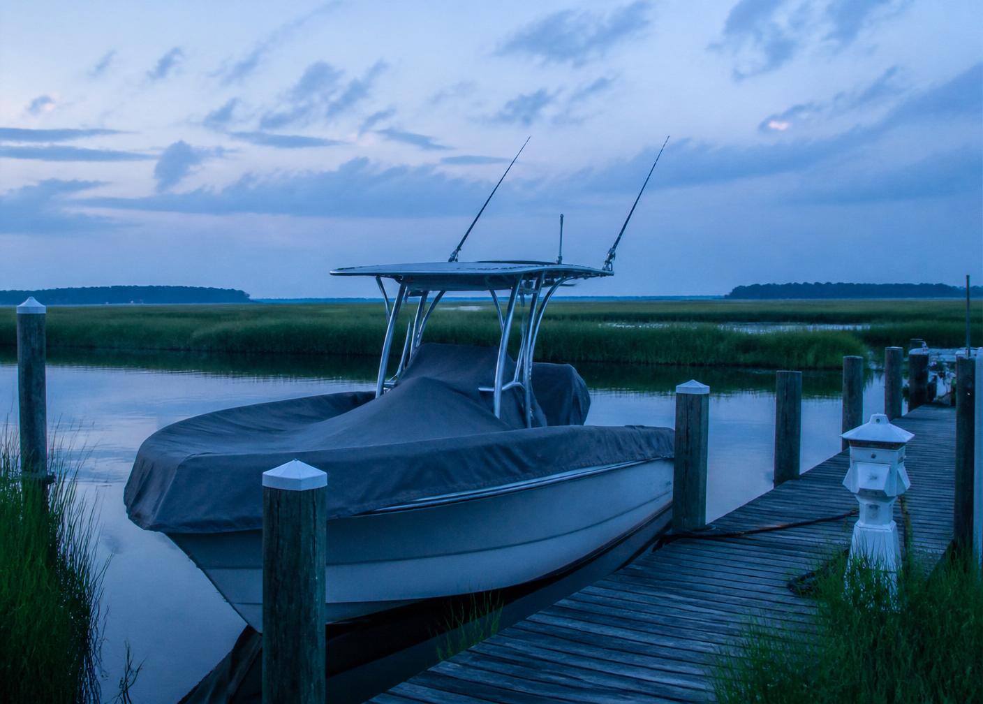 Center console boat covered at a private dock beside marsh grass at dawn